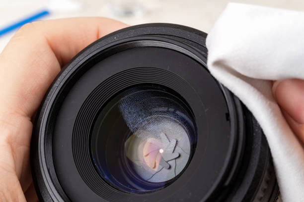 istock Fingerprint on a front camera lens close-up. Hands wiping a lens rim with a microfiber cloth before cleaning the greasy stain on a lens. Maintenance of photographic equipment. 1281038251