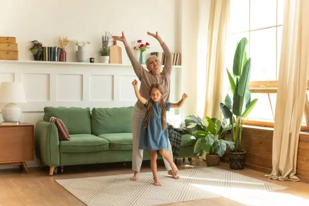 Photo of Energetic senior female grandma dancing together with granddaughter in living room.