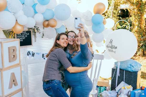 Female friends taking selfie with pregnant woman at a baby shower Female friends taking selfie with pregnant woman at a baby shower. Mobile photography, party decorations in white and blue colors, baby boy baby shower stock pictures, royalty-free photos & images
