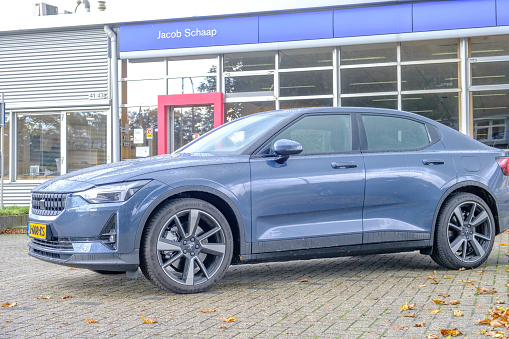 Dronten, The Netherlands - October 9, 2020: Polestar 2 all-electric 5-door fastback car side view in blue parked in front of a Volvo dealership in Dronten, Flevoland, The Netherlands. Polestar is the performance company and brand of Volvo Cars now focussed on producing electric and hybrid vehicles. The Polestar 2 is powered by two electric motors driving the front and rear wheels.