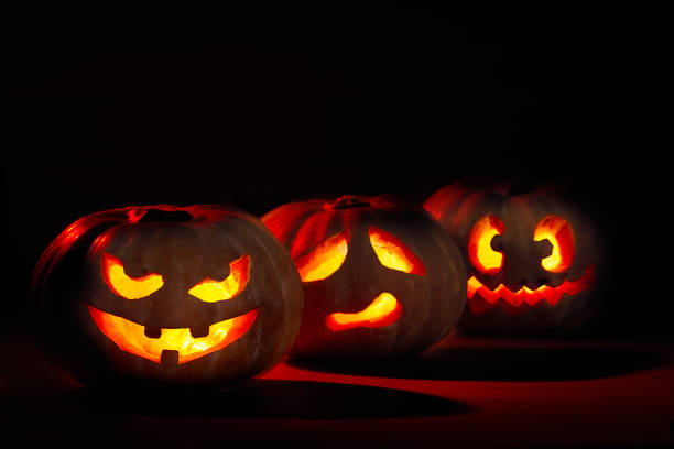 istock Three illuminated halloween pumpkins. With devilish, sad and crazy face on dark background with red light 1281048112