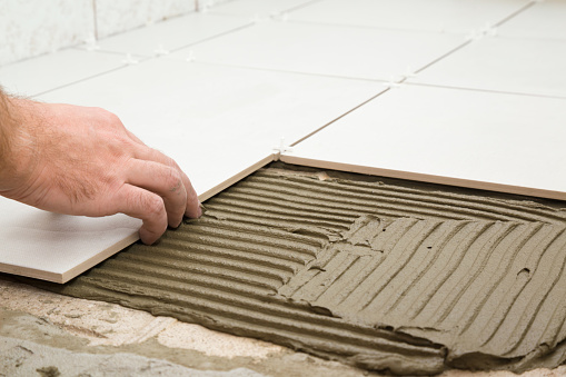 Worker hands gluing white ceramic tiles on floor. Closeup.