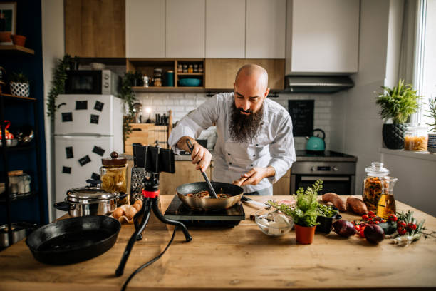 Cooking for internet vlogg Young bearded hipster chef, food vlogger filming and live streaming steak preparing tutorial in home kitchen tutorial photos stock pictures, royalty-free photos & images