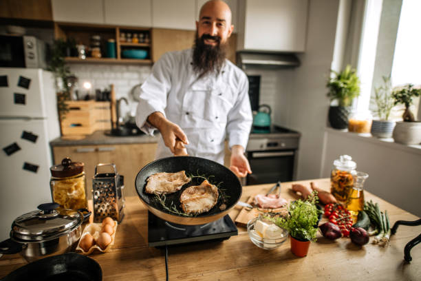 Passionate young man cooking Young bearded man preparing healthy lunch from organic ingredients at home kitchen. Frying meat chop and making rucola salad cooking show stock pictures, royalty-free photos & images