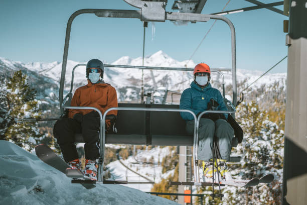 two skiers with mouth nose mask on chair lift two skiing people, man and woman wearing mouth nose mask on chair ski lift with social distance on sunny winter day in the mountains ski lift photos stock pictures, royalty-free photos & images