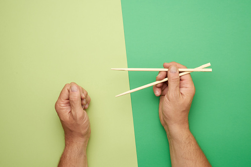 Pair of wooden chopsticks in a male hand on a green background, top view