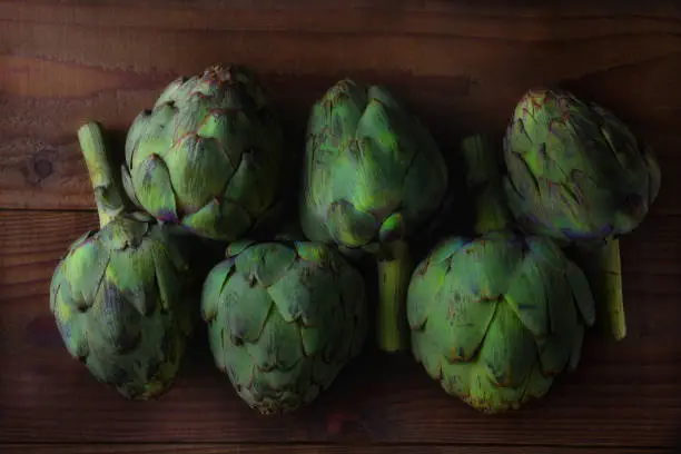A group of 6 fresh picked artichokes on a rustic dark wood table.
