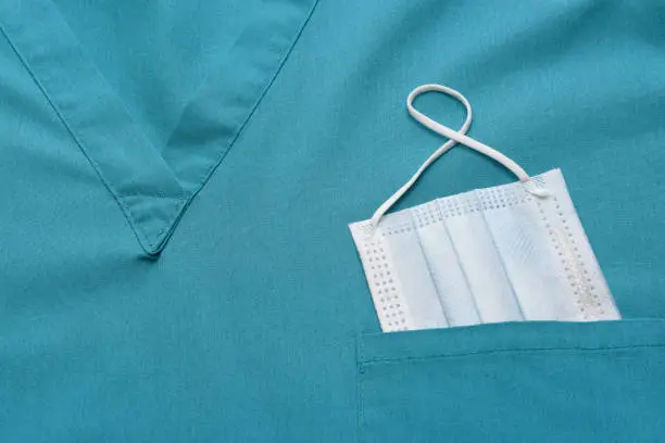 Closeup of a medical scrubs top with a surgical mask in the pocket.