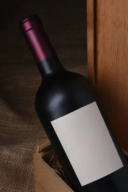 Closeup of a red wine bottle in a wooden box. Bottle has a blank label