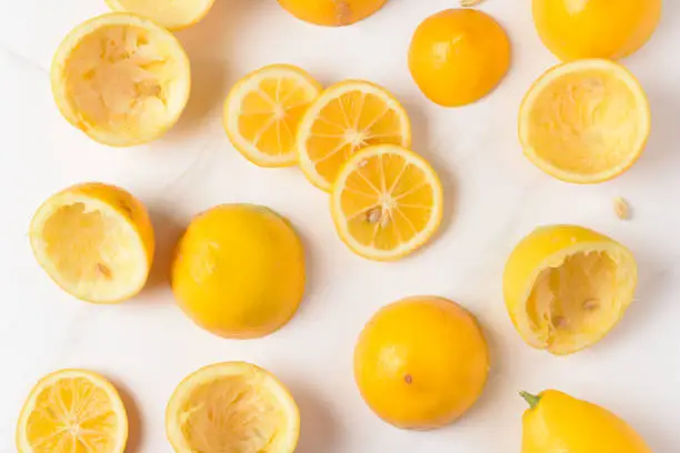 High angle shot of lemon rinds, whole lemons and lemon slices on a white marble kitchen surface.