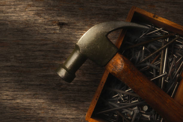 Tool Still Life: An old hammer resting on top of a wood box of assorted nails on a rustic workbench. High angle shot with strong, warm side light.
