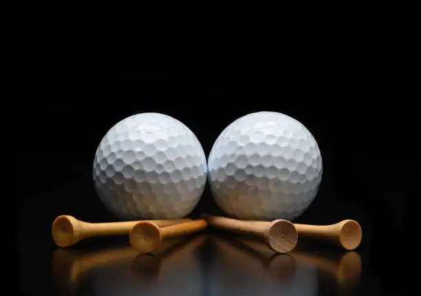 Golf Still Life. Two golf balls with tees laying on a black reflective surface. Low angle with copy space.