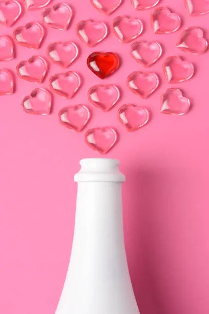 Valentines Day Concept: high angle shot of a white champagne bottle with pink glass hearts simulating a spray.