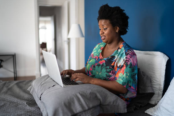 istock Woman sitting on bed using laptop 1281073862