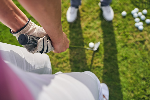 Cropped photo of a Caucasian lady golfer and her trainer practicing a putting stroke technique