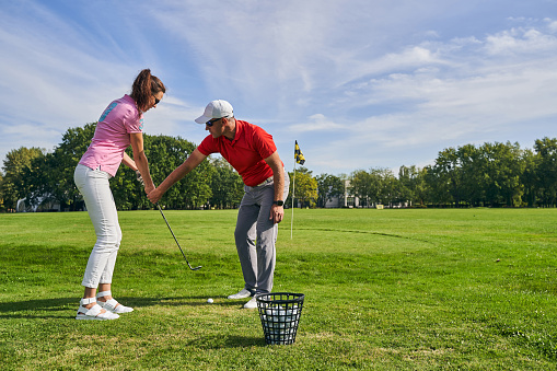 Experienced male instructor teaching a young woman to hold a club correctly during the game