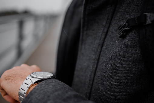 Close up of a man in formal clothes looking at the watch while waiting for someone outside in bad weather.