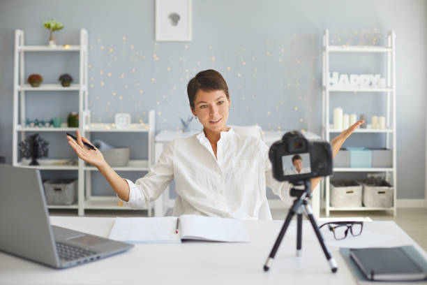 vlogger feminino confiante gravando vídeo na câmera sentado em sua mesa em aconchegante home office - video sharing - fotografias e filmes do acervo