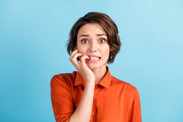 oh no i failed again. closeup photo of sad terrified lady horrified facial expression made big mistake feel guilty bite lips fingers wear orange shirt isolated blue color background - nail biting imagens e fotografias de stock