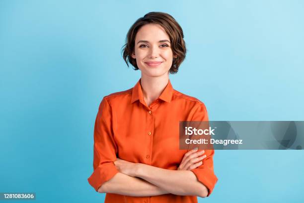 Photo Of Attractive Charming Lady Cute Bobbed Hairdo Arms Crossed Selfconfident Person Worker Friendly Smile Good Mood Wear Orange Office Shirt Isolated Blue Color Background Stock Photo - Download Image Now