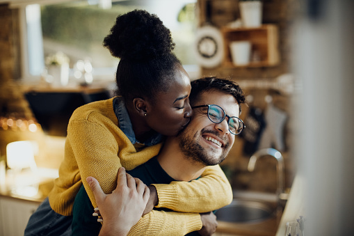 Young African American woman kissing her boyfriend having fun with him at home.