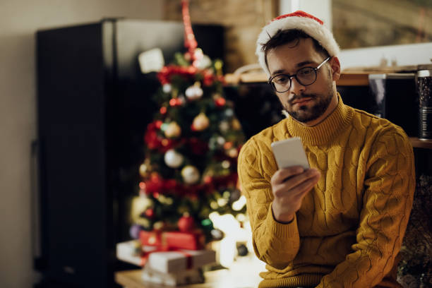 istock Young distraught man reading text message on cell phone while being alone at home on Christmas. 1281085743