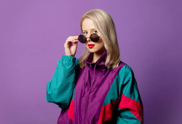 Style blonde in 80s windbreaker and roud sunglasses on purple background Style blonde in 80s windbreaker and roud sunglasses on purple background wind shelter stock pictures, royalty-free photos & images