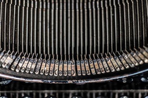 A close-up of a very old and worn typewriter with linen paper for copy space. Black background and full frontal view.