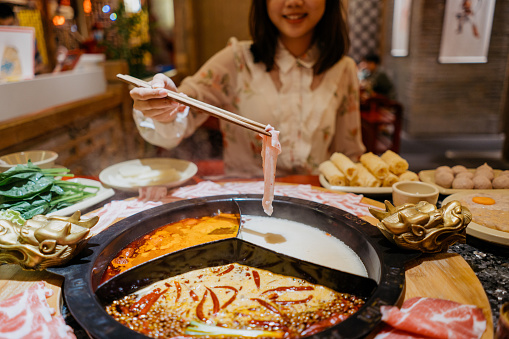 An Asian Chinese woman boiling a pork slice with hot pot soup
