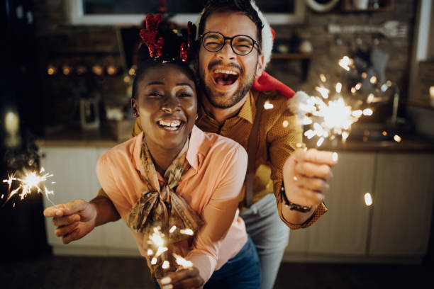 Festive couple having fun while celebrating New year at home. Young cheerful couple having fun with sparklers on New Year's eve at home. new years eve parties stock pictures, royalty-free photos & images