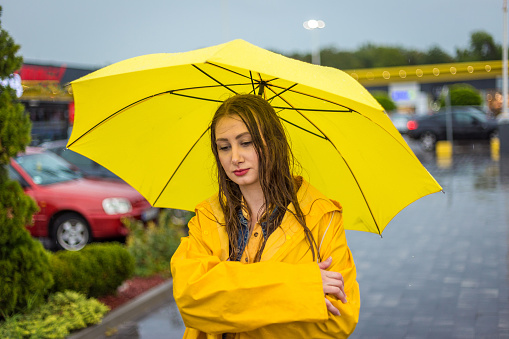 Portrait of preteen girl in yellow raincoat and umbrella smiling and looking at camera outdoors in autumn.