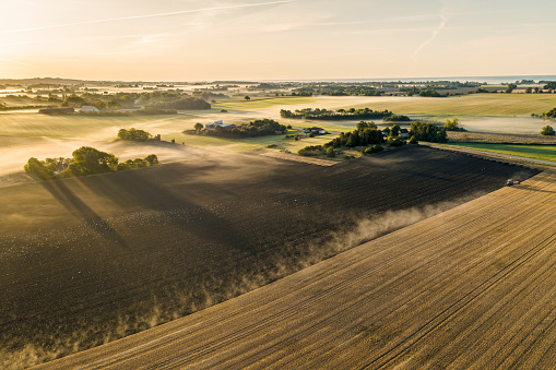 Drone view of a farmer ploughing a field in the early morning with mist hanging in the air. Photographed on the island of Moen in Denmark. Colour, horizontal with some copy space.