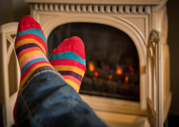 Warming feet by the fire Close-up of a man's colourful socks as he warms his feet by a traditional styled gas stove. heat home interior comfortable human foot stock pictures, royalty-free photos & images