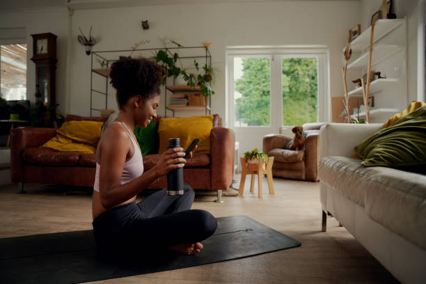 istock Smiling young african woman holding bottle and using smartphone during workout while sitting on fitness mat at home 1281096653