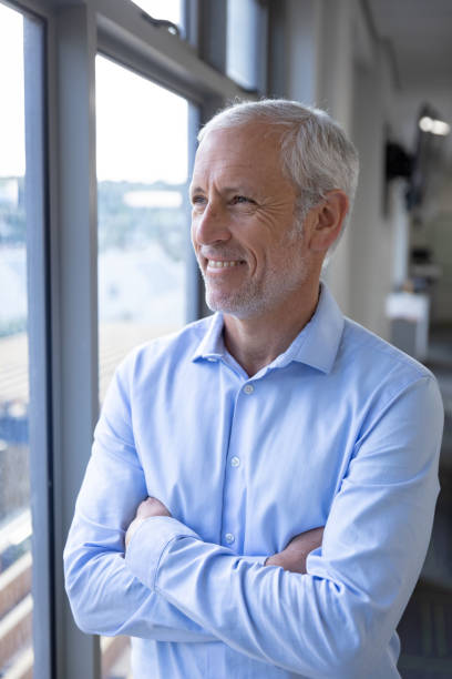 istock Senior businessman smiling while looking through window at modern office 1281099807