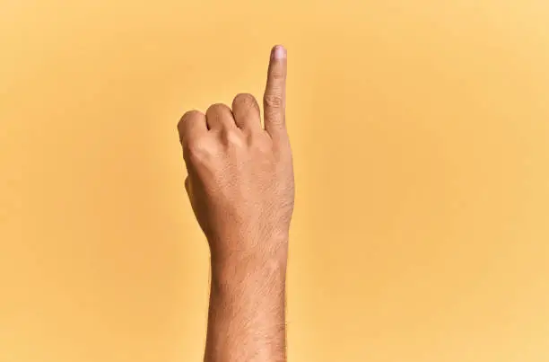 Photo of Arm and hand of caucasian man over yellow isolated background showing little finger as pinky promise commitment, number one