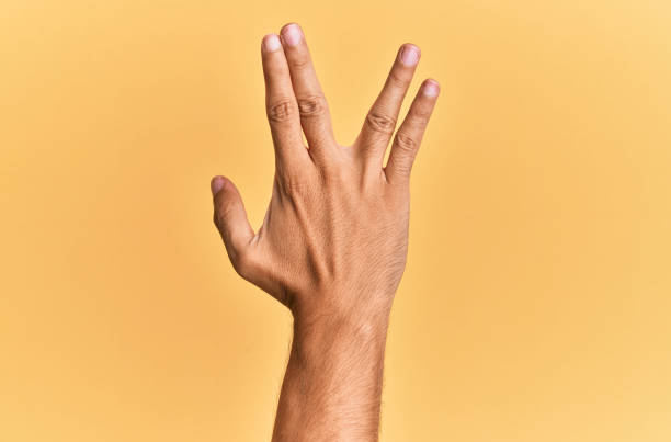 Arm and hand of caucasian man over yellow isolated background greeting doing vulcan salute, showing back of the hand and fingers, freak culture Arm and hand of caucasian man over yellow isolated background greeting doing vulcan salute, showing back of the hand and fingers, freak culture vulcan salute stock pictures, royalty-free photos & images