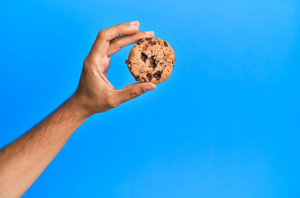 istock Hand of young hispanic man holding chocolate cookie over isolated blue background. 1281100593