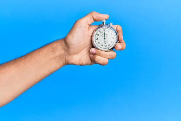 Photo of Hand of young hispanic man using stopwatch over isolated blue background.