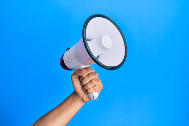istock Hand of hispanic man holding megaphone over isolated blue background. 1281100762