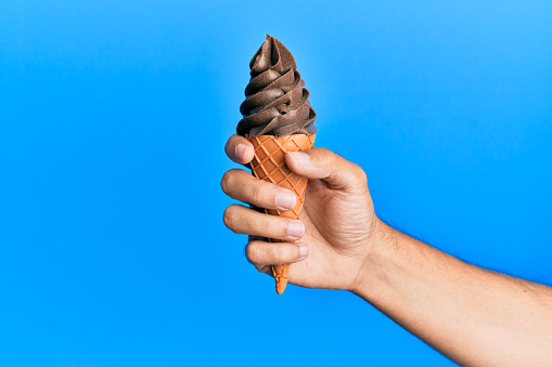 Hand of hispanic man holding ice cream over isolated blue background.