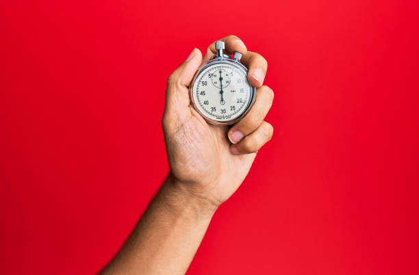 mão de jovem hispânico usando cronômetro sobre fundo vermelho isolado. - stopwatch - fotografias e filmes do acervo