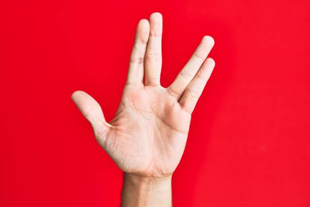 Arm of caucasian white young man over red isolated background greeting doing vulcan salute, showing hand palm and fingers, freak culture Arm of caucasian white young man over red isolated background greeting doing vulcan salute, showing hand palm and fingers, freak culture vulcan salute stock pictures, royalty-free photos & images
