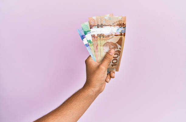 istock Hispanic hand holding canadian dollars banknotes over isolated pink background. 1281101488