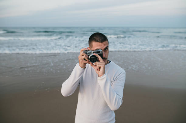 istock Young man taking a picture with a vintage camera by the sea 1281103252