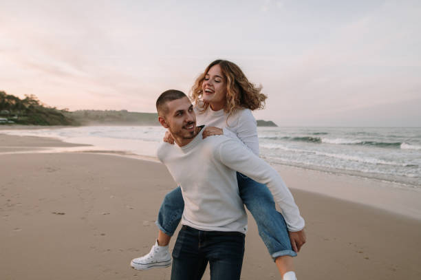 istock Young couple walking piggyback on a beach at sunset 1281103922