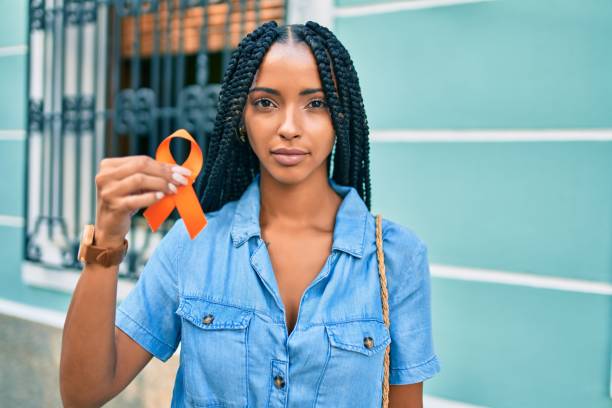 junge afrikanische amerikanische frau mit entspanntem ausdruck hält orange band an der stadt. - multiple sklerose stock-fotos und bilder