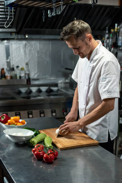 istock Young professional chef of modern restaurant in white uniform cutting onion 1281105037