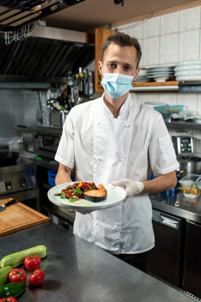 istock Male chef holding fried salmon with steamed vegetables over kitchen table 1281105040