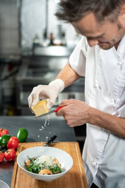 istock Professional young chef in uniform grating cheese into ceramic bowl with salad 1281105050